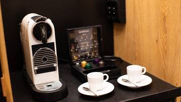 A coffee machine with a control panel, two white cups with saucers, and a tray with colorful capsules.