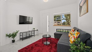 Un salon moderne avec un canapé gris, un tapis rouge et un téléviseur fixé au mur.