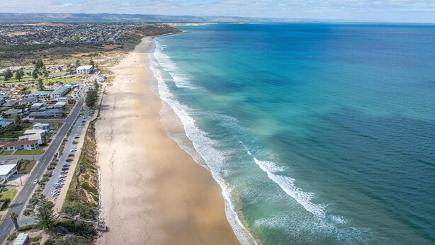 Vue aérienne d’une ville côtière avec une longue plage de sable, une route parallèle à la côte et des immeubles d’habitation.