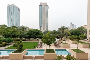 A hotel with a pool area, palm trees, and high-rise buildings in the background. - Lux BnB Greens & Views Lake View  (Dubai)