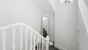 Un escalier blanc avec une rampe, menant à un palier agrémenté d’un miroir et d’un porte-manteau.