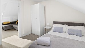 Une chambre à coucher avec un lit, un canapé gris, une armoire et une petite table de chevet avec une lampe.