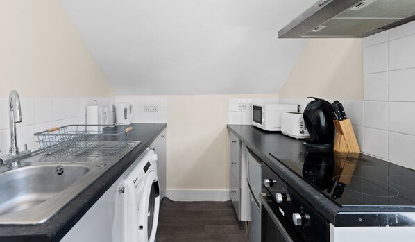 Una kitchenette compacta con lavamanos, escurreplatos, microondas, tostadora y cafetera.