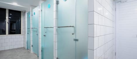 A row of glass-enclosed restrooms with a tiled floor and a white wall with a security camera.