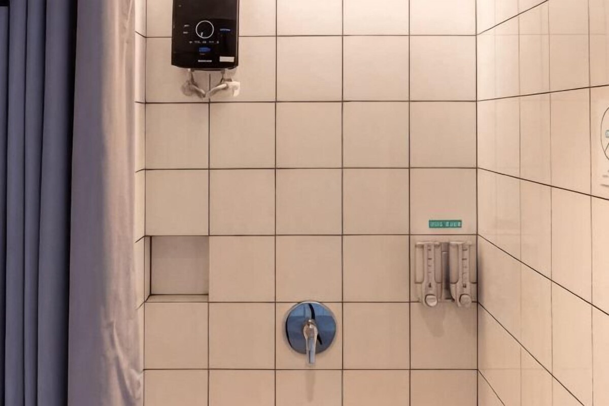 Pared de azulejos con un panel de control, inodoro azul y un cartel que indica baño de hombres.