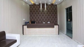 A reception area with a wooden reception desk, vertical striped wallpaper, and a glass door leading to another room. - Hotel Airport Sinon by Dream Laxmi (New Delhi)