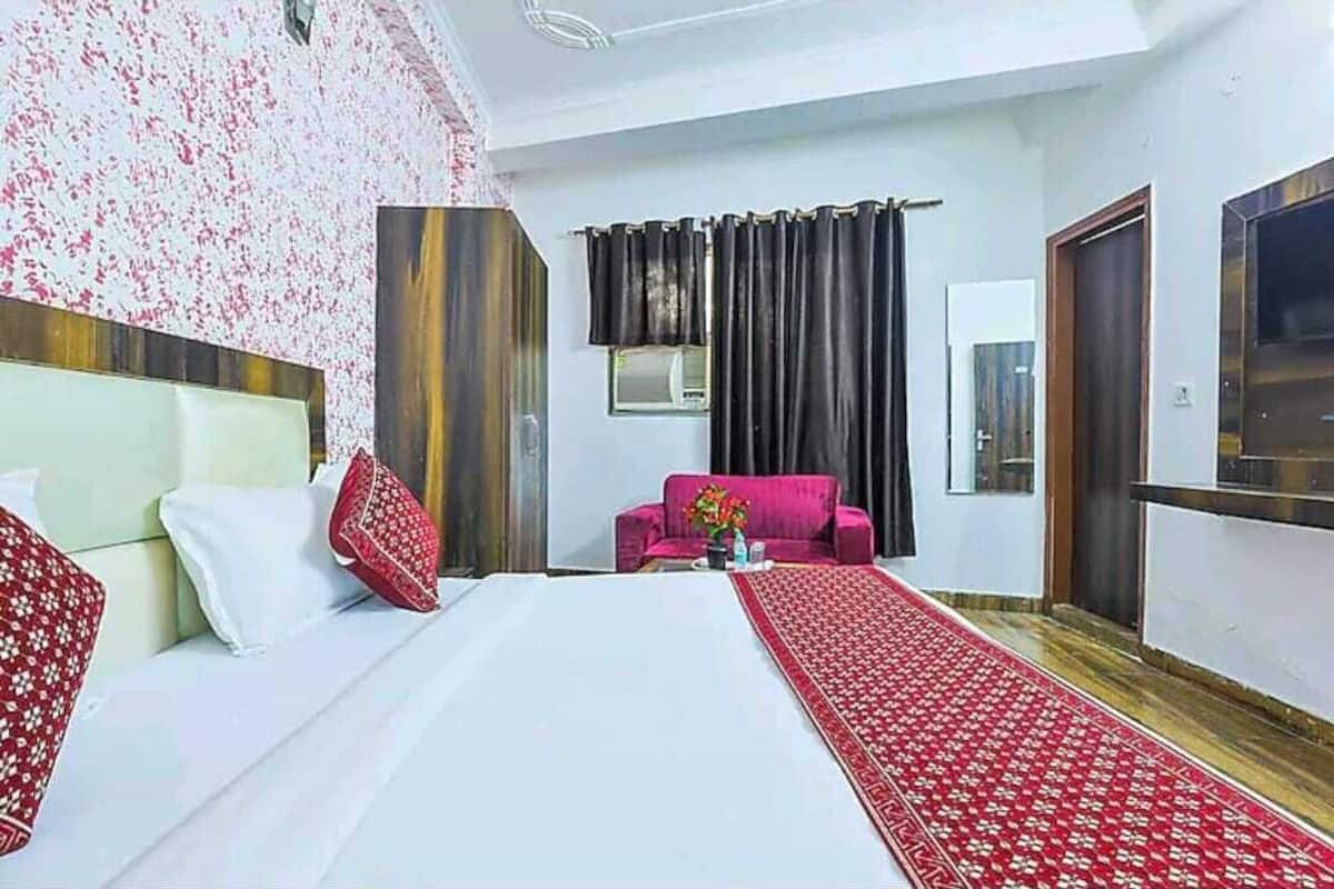 Ein Hotelzimmer mit einem Bett, einem roten Sofa, einem Fernseher und einem Fenster mit Vorhängen.