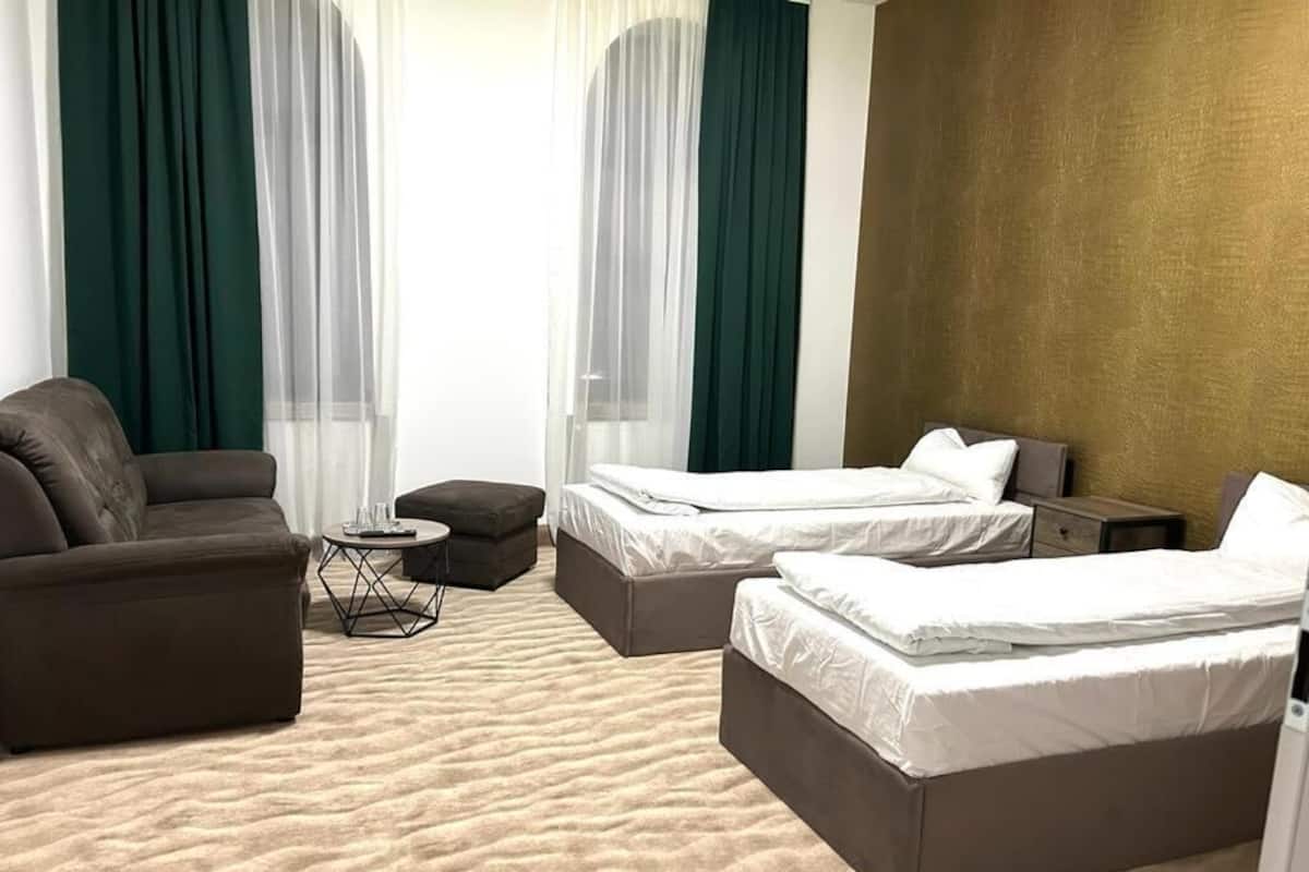 A hotel room with two beds, a sofa, a small table, and sheer curtains.