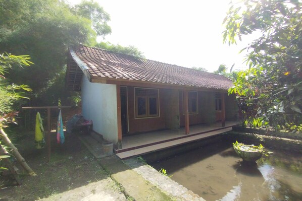 A small house with a tiled roof, a front porch, and a small pond in the yard. - Hotel O Dannis Homestay Near Musholla Al Istiqomah Terawangan (Narmada)