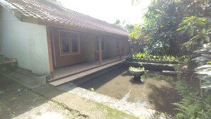 A traditional building with a tiled roof, a small water feature, and a garden with various plants. - Hotel O Dannis Homestay Near Musholla Al Istiqomah Terawangan (Narmada)