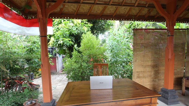 A wooden table with a laptop, surrounded by plants and a bamboo fence. - Hotel O Dannis Homestay Near Musholla Al Istiqomah Terawangan (Narmada)