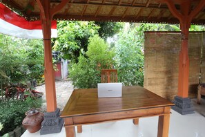 A wooden table with a laptop, surrounded by plants and a bamboo fence. - Hotel O Dannis Homestay Near Musholla Al Istiqomah Terawangan (Narmada)