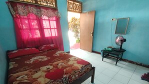A bedroom with a bed, a fan, a table, and a door leading outside. - Hotel O Dannis Homestay Near Musholla Al Istiqomah Terawangan (Narmada)