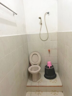 A small bathroom with a toilet, a shower, and a trash bin. - Hotel O Sederhana Homestay (Sidoarjo)