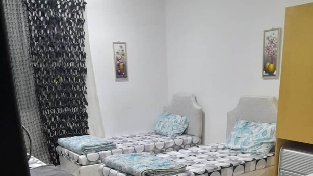 Ein Zimmer mit zwei Betten, einem kleinen Tisch mit einem Topfpflanzen und einem Vorhang mit Blattmuster.