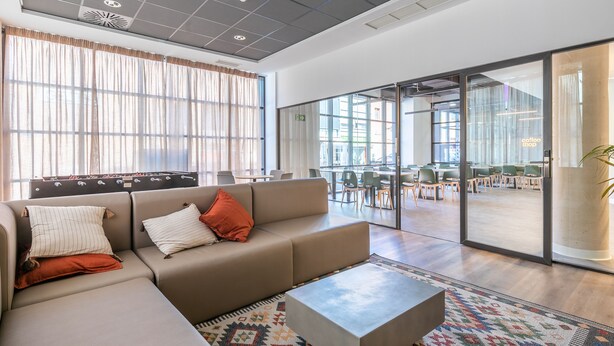 A modern lounge area with a sofa, a coffee shop sign, and a view of the dining area. - Micampus Estrada 11 (Madrid)