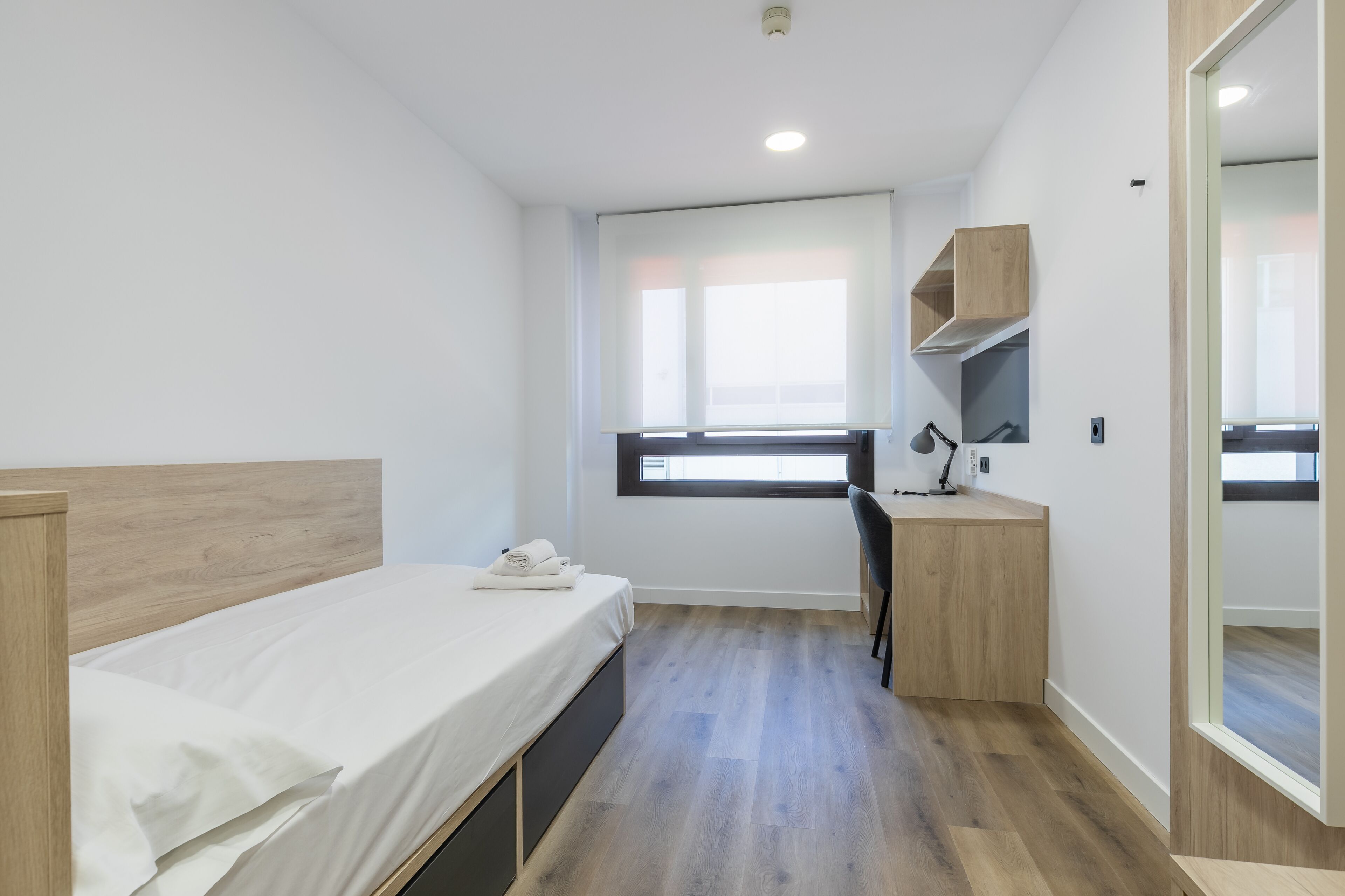 A compact hotel room with a single bed, a desk, and a chair.