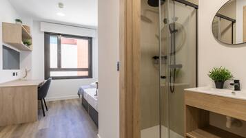 A modern bathroom with a glass shower enclosure, a wooden vanity, and a small potted plant.