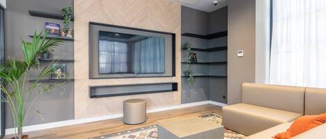 Una sala de estar moderna con un sofá, una mesa de centro, un televisor montado en la pared y plantas decorativas.