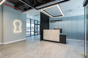 Ein moderner Empfangsbereich mit minimalistischem Design, der einen Empfangstresen, eine lichtinstallation in Schlüsselform und einen Ausblick ins Freie durch große Fenster bietet.
