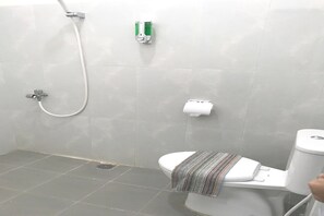 Casa de banho com chuveiro, sanita e um porta-toalhas.