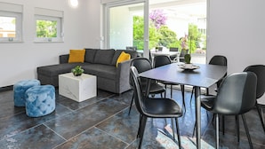 A modern living room with a grey sofa, blue ottomans, a white marble coffee table, and a dining area with a black table and chairs. - Pool apartments Banta A (Novalja)