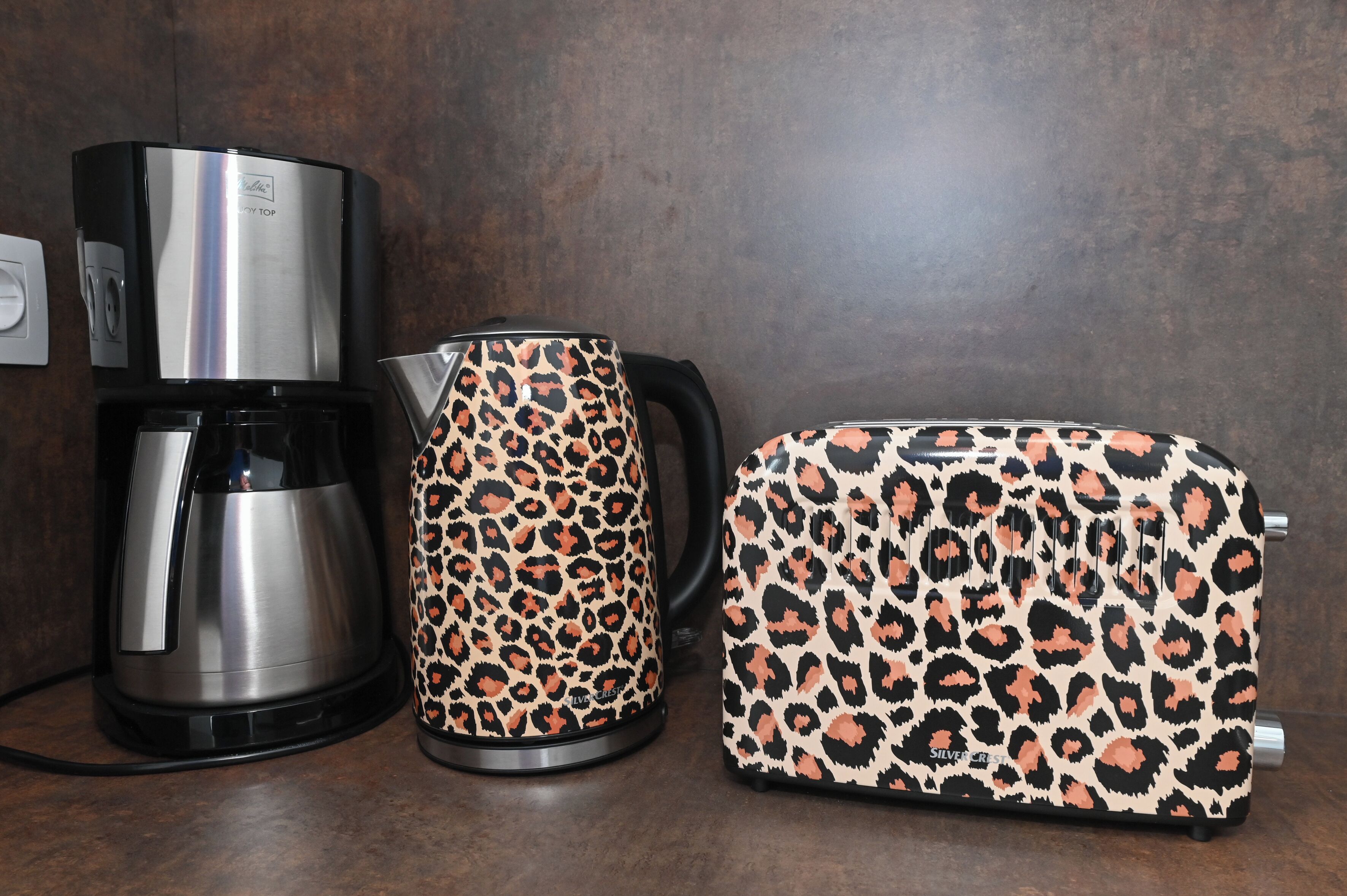 Une machine à café, une bouilloire et un sac à motifs léopard posés sur un plan de travail.