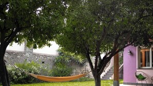 A hammock in a grassy area with trees, a stone wall, and a purple building with a staircase.