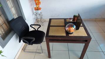 A small room with a tiled floor, a black office chair, a wooden table with a laptop, a potted plant, and a decorative glass bowl.