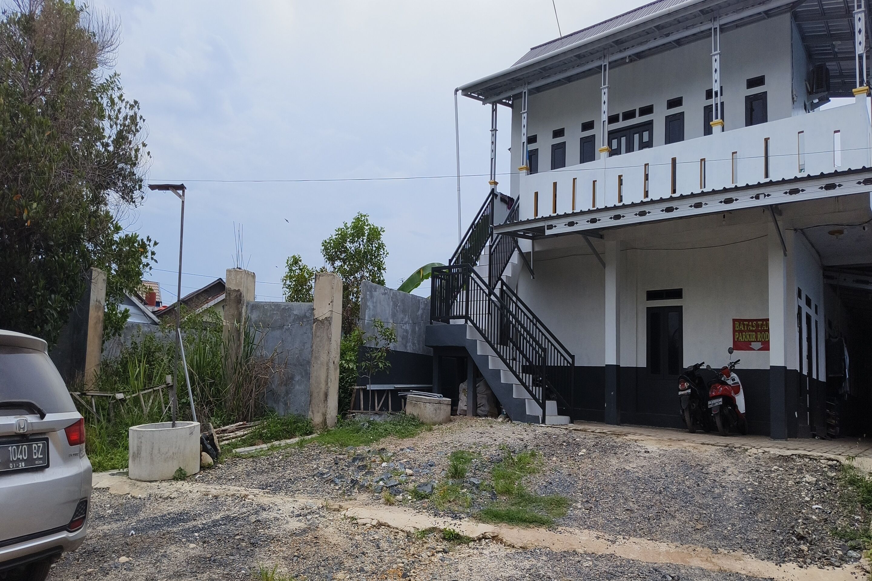 A building with a staircase leading to a second floor, a sign indicating a parking area, and a parked car.