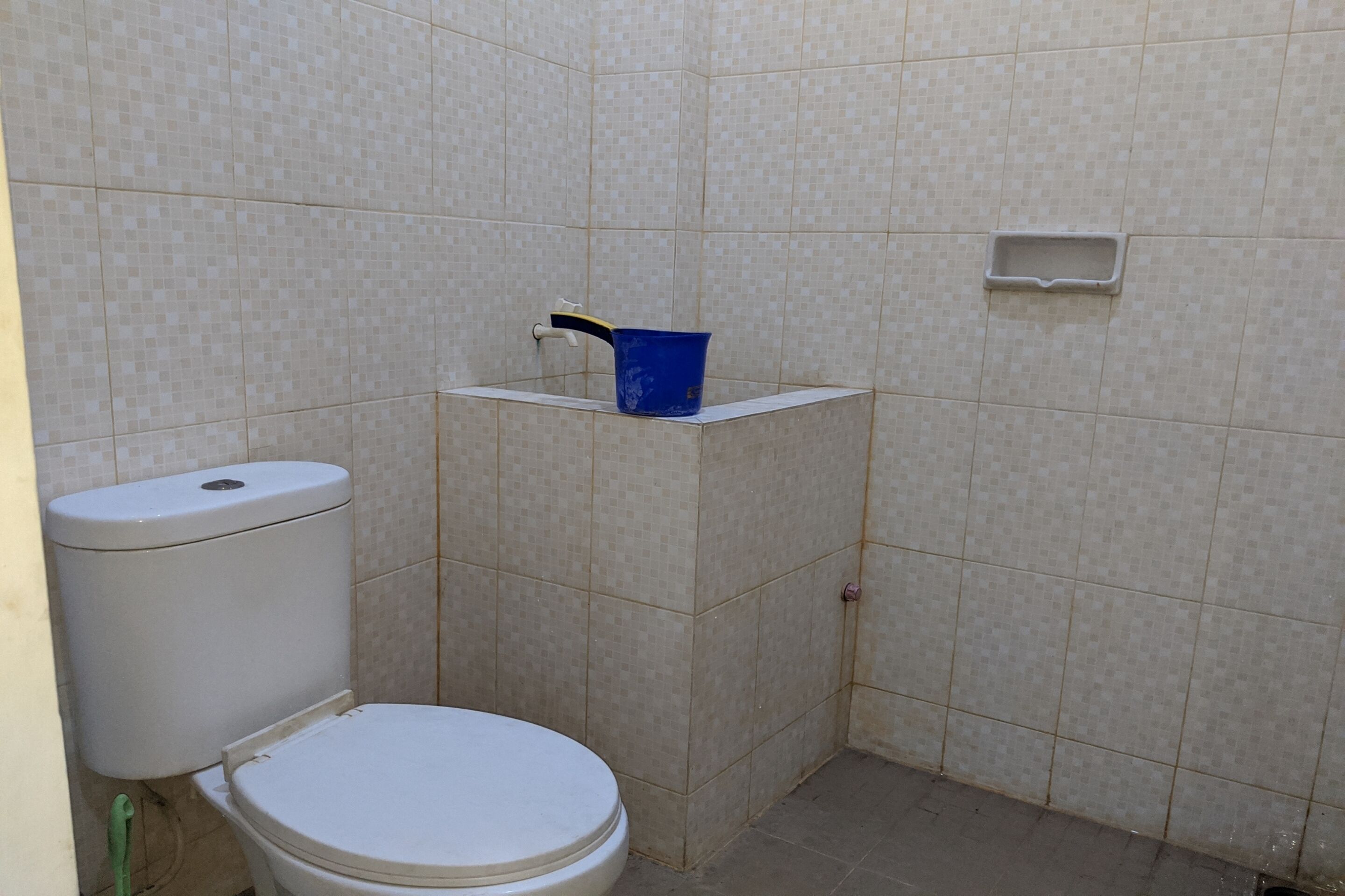Un baño pequeño con un inodoro, un cubo azul sobre una repisa y un jabonera en la pared.