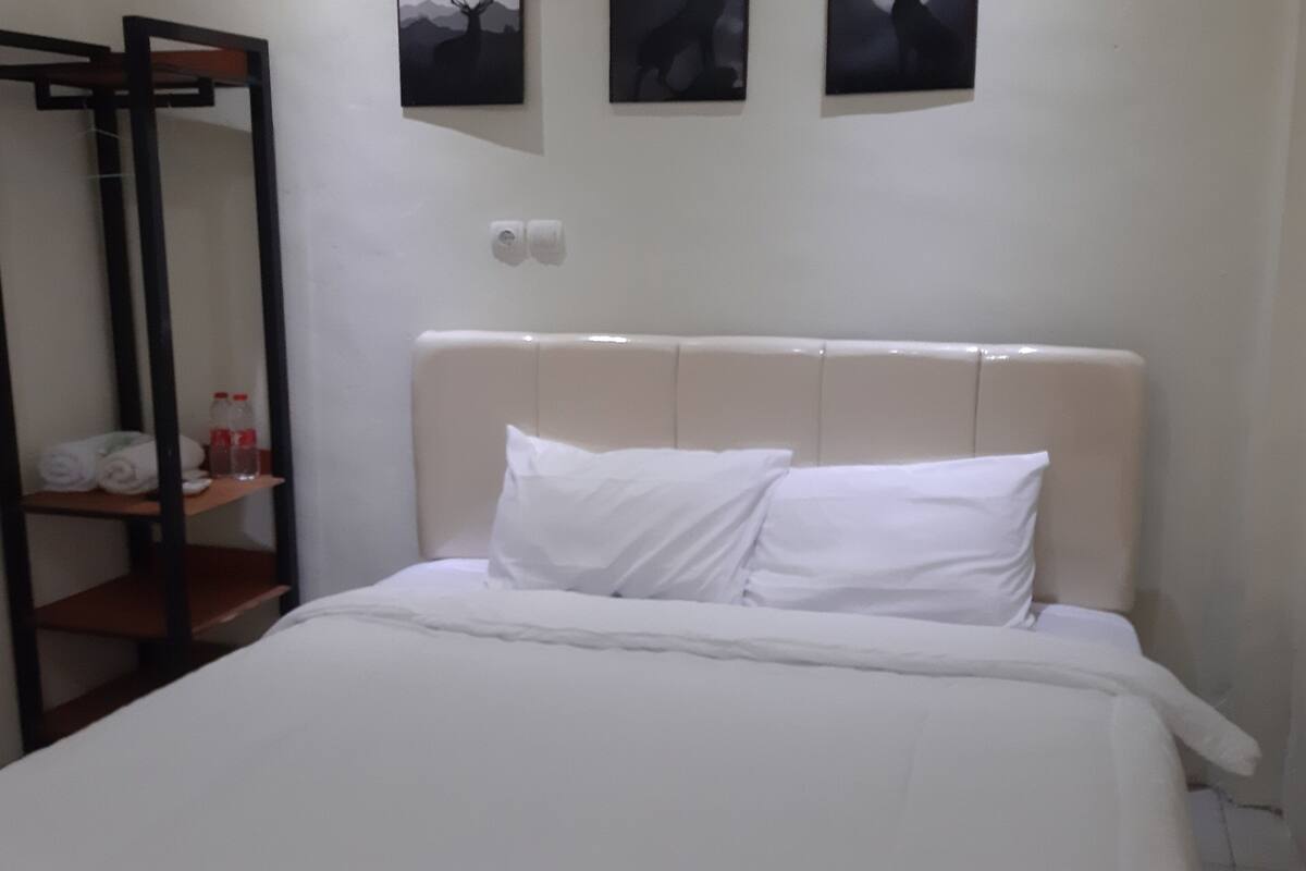 A hotel room with a bed, a wooden shelf with towels and toiletries, and three framed pictures on the wall.
