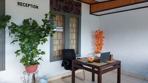 A reception area with a reception desk, a potted plant, a chair, and a window with a sign. - Hotel O Penginapan Al-asharNearWarung Acil Ubai (Boemirata)