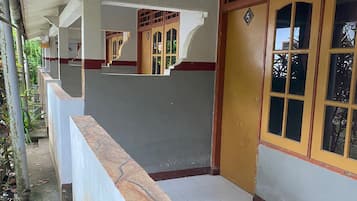 A corridor with a tiled floor, a white railing, and a door with a number plate.
