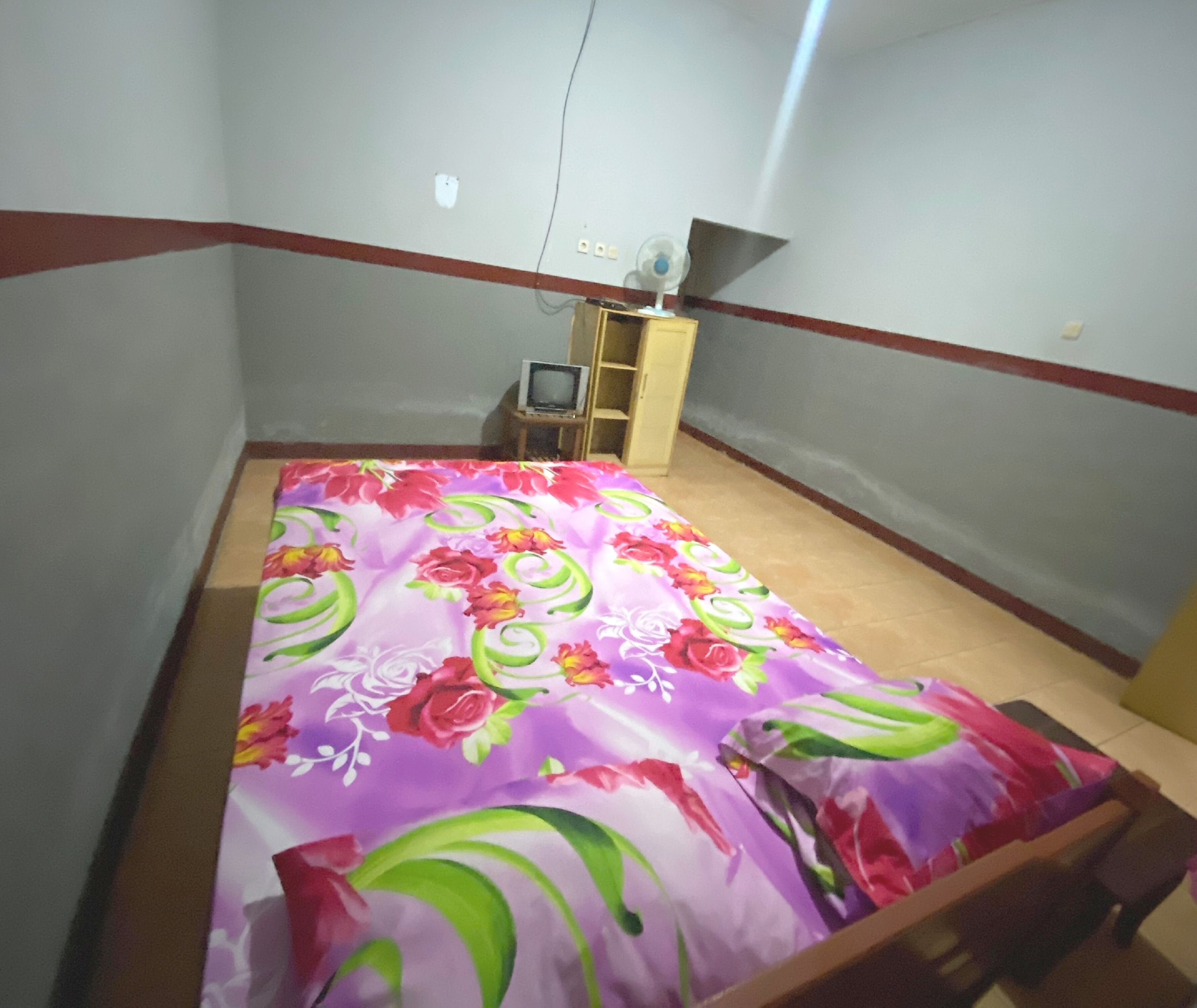 A small bedroom with a bed, a TV, and a wooden cabinet.