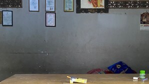 Un comptoir d’accueil avec un tableau encadré au-dessus, plusieurs documents encadrés accrochés au mur et une petite poubelle sur le comptoir.