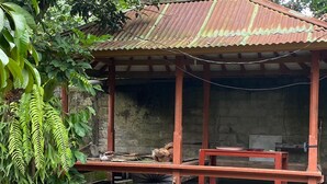 Une structure rustique en bois, surmontée d’un toit en métal ondulé, avec un banc et un seau.