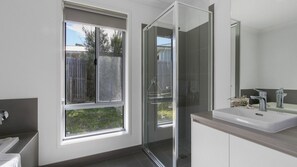 Bathroom features a glass shower enclosure, white sink, and dark-toned vanity with a view of the outdoors.