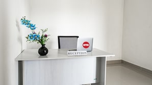 Un comptoir d’accueil avec un ordinateur portable, un vase de fleurs et une pancarte indiquant « RÉCEPTION ».