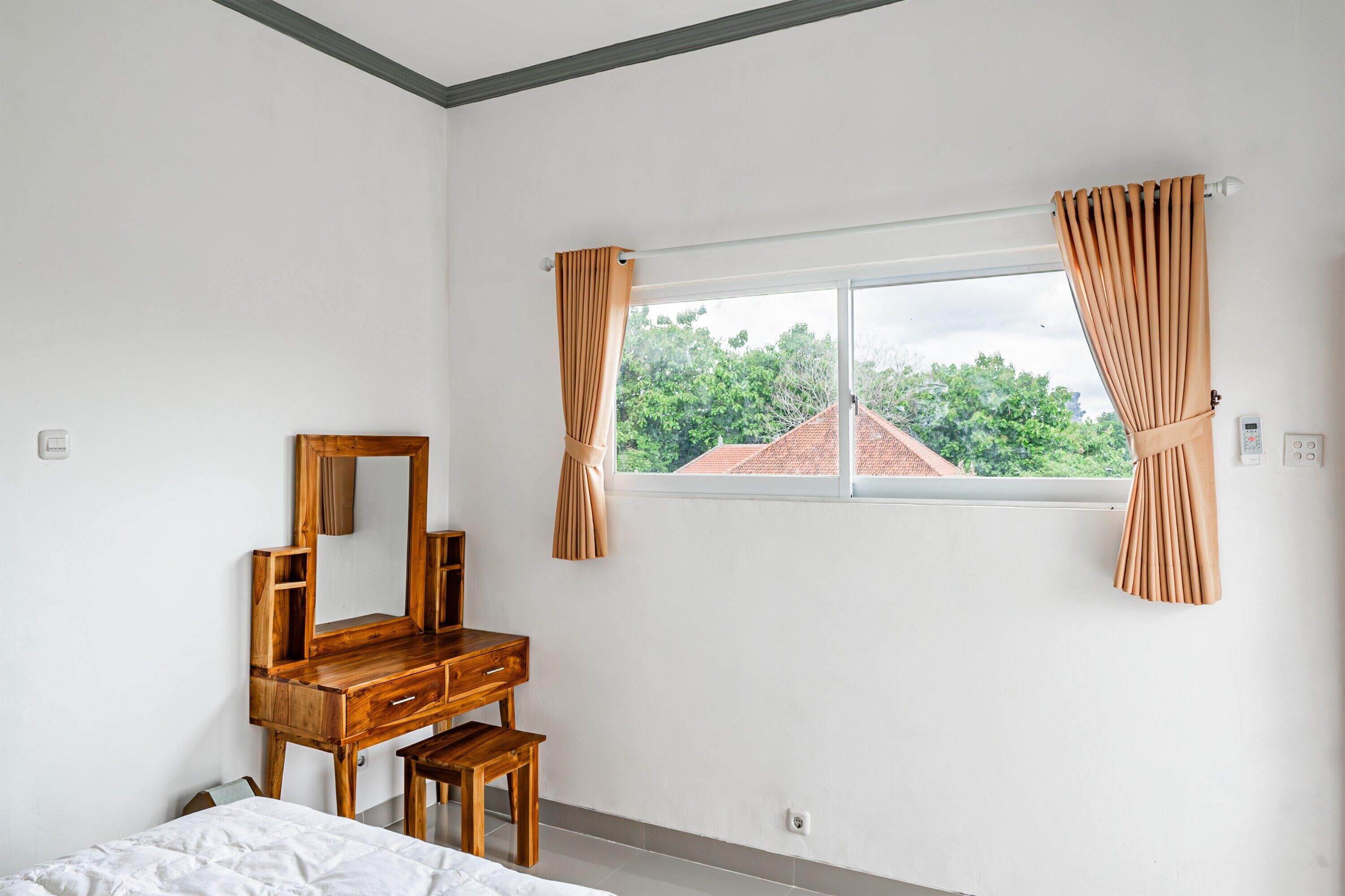 A bedroom with a wooden dresser, a bed, and a window with curtains.
