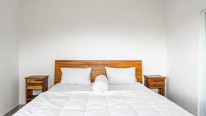Un lit bien fait, avec une tête de lit en bois, deux tables de chevet et un oreiller blanc.
