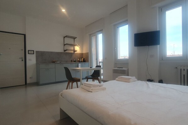 A modern hotel room with a bed, a desk, a chair, a TV, and a view of the city. - BnButler - 48 Monza Ave. (Milano)