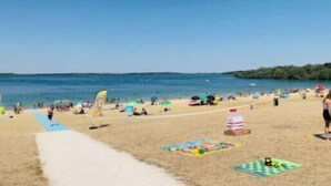 Ein Strand mit Menschen, einem Rettungsturm und blauem Himmel.