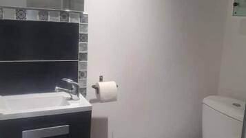 Un baño con lavamanos blanco, un inodoro y un cubo de basura pequeño.
