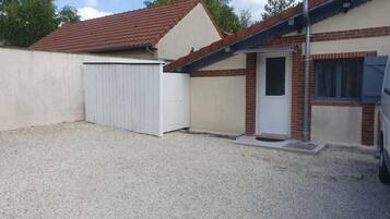 Un bâtiment d’un seul étage, avec un toit recouvert de tuiles rouges, une porte de garage blanche et une petite porte d’entrée.
