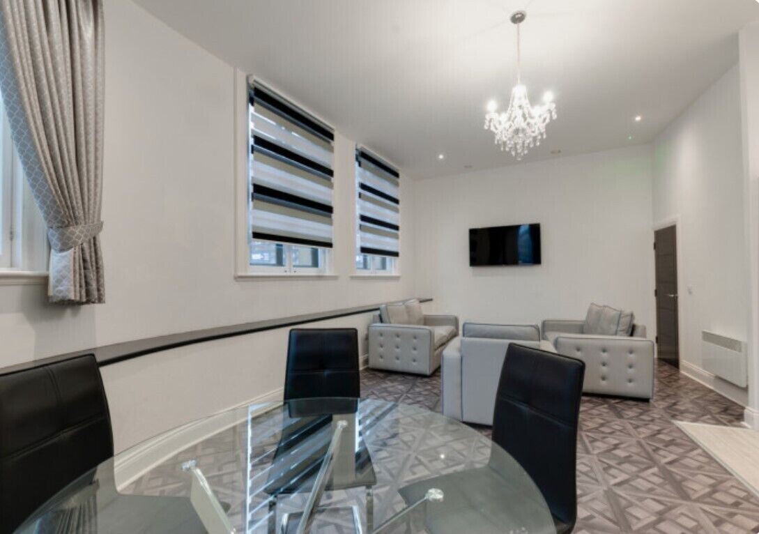 Uma sala de estar moderna com uma mesa de jantar de vidro, sofás e um candeeiro.