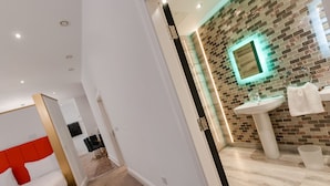 A modern hotel room with a large bed, a bathroom with a tiled wall, a sink, and a mirror.