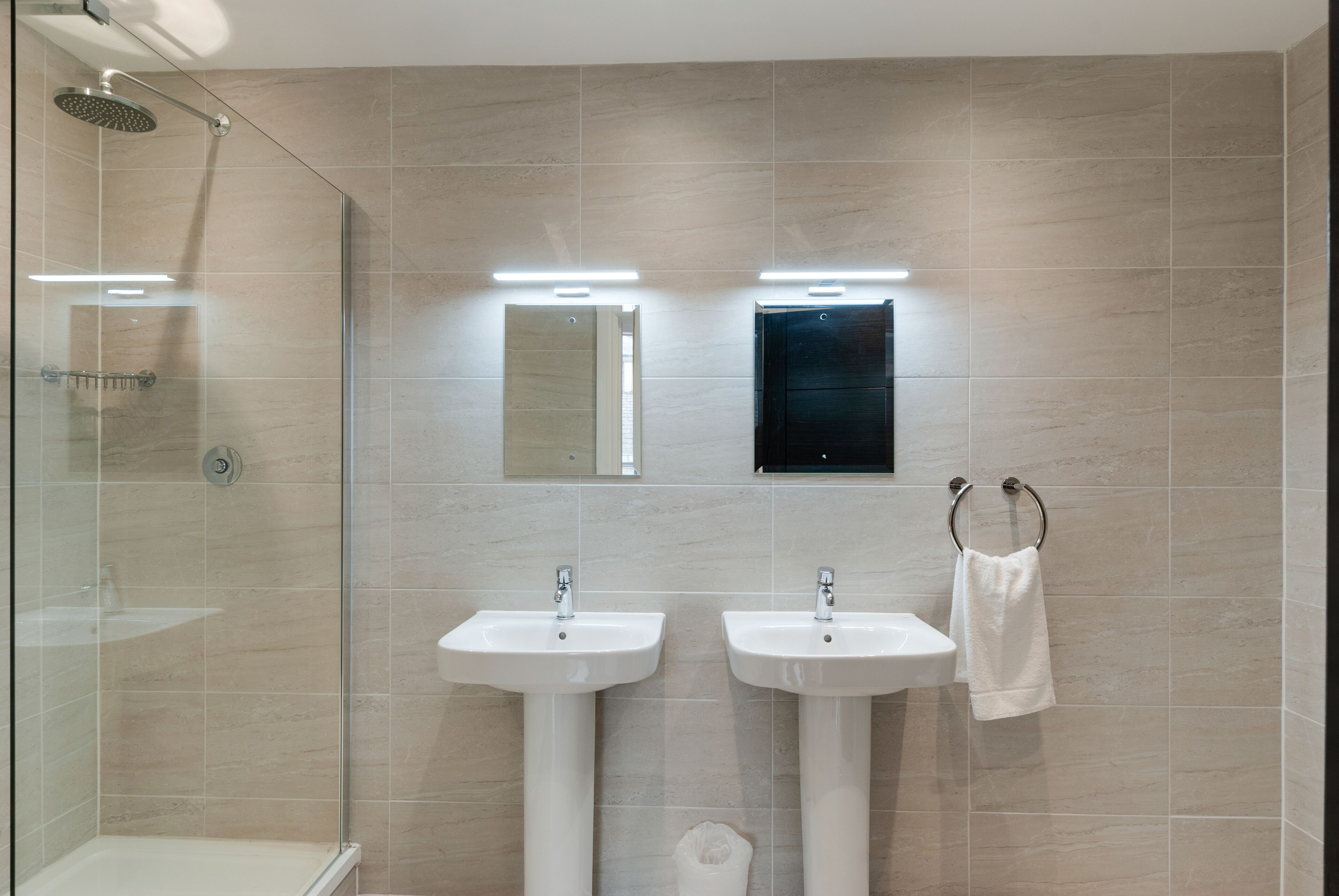 Ein modernes Badezimmer mit zwei Waschbecken, einer Glasdusche und einem Handtuchhalter.