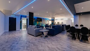 A spacious living area with a modern design, featuring a large sofa set, a coffee table, and a dining table with chairs.