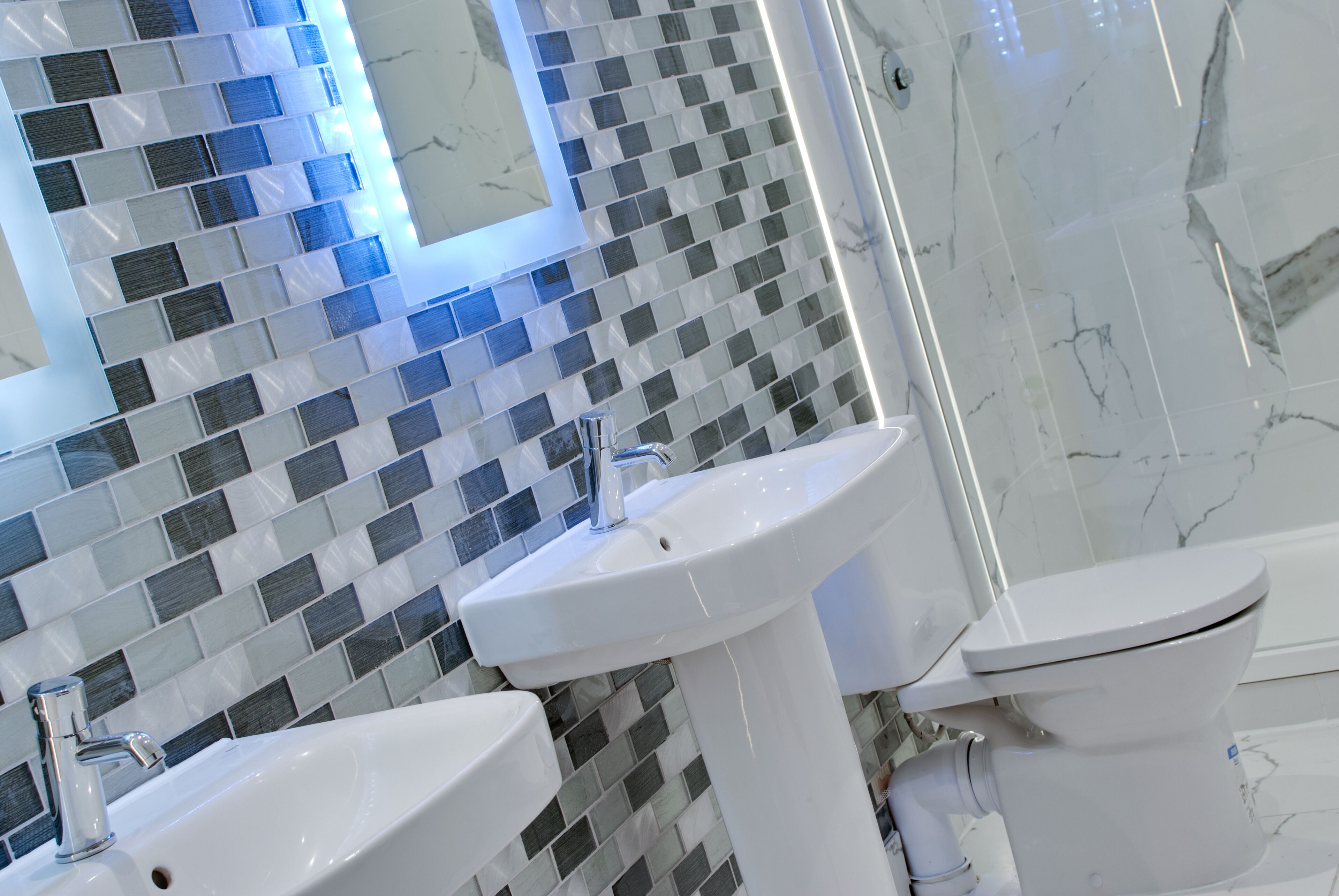 Casa de banho com painel de azulejos, duas pias e uma sanita.